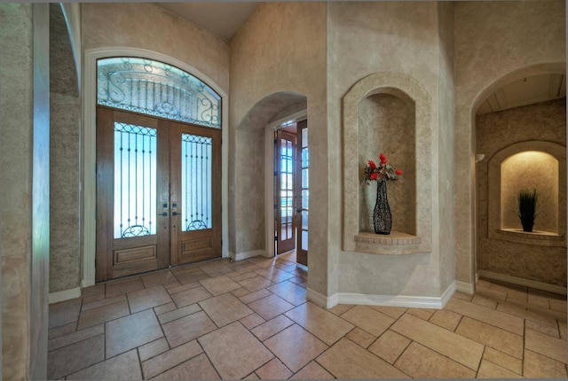 entrance foyer featuring french doors, stone tile floors, a towering ceiling, and baseboards