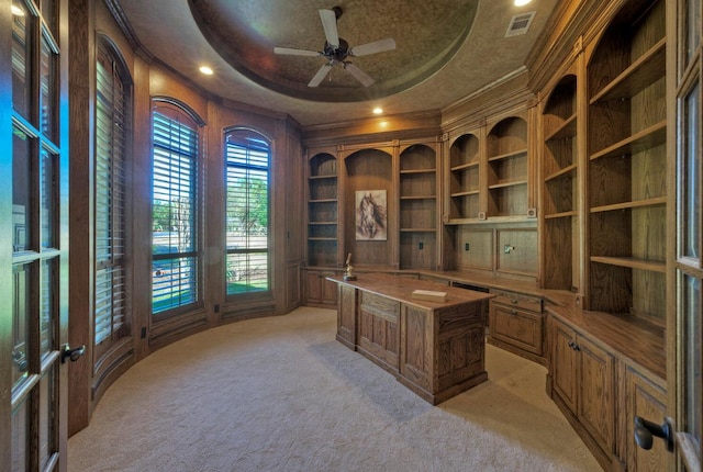 office space with light carpet, visible vents, a ceiling fan, ornamental molding, and a raised ceiling