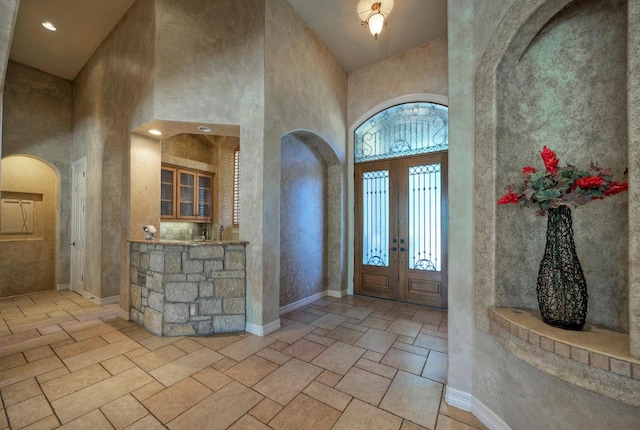 foyer entrance with arched walkways, plenty of natural light, a towering ceiling, and baseboards