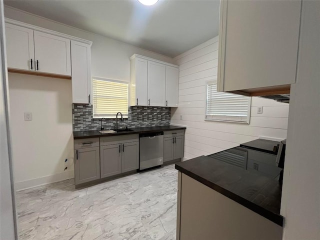 kitchen featuring a sink, marble finish floor, stainless steel dishwasher, tasteful backsplash, and dark countertops