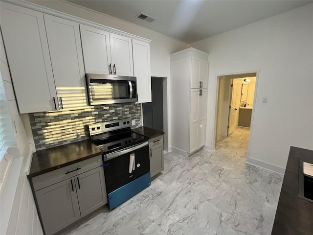 kitchen with visible vents, dark countertops, marble finish floor, stainless steel appliances, and backsplash