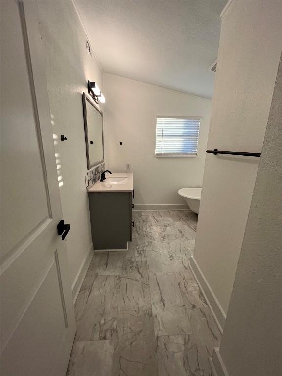 full bath with a freestanding bath, marble finish floor, vanity, and baseboards