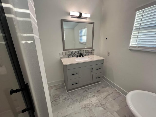 bathroom featuring marble finish floor, baseboards, a freestanding bath, and vanity