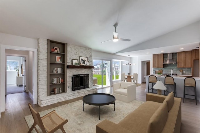 living room featuring light wood-style floors, a fireplace, vaulted ceiling, and ceiling fan with notable chandelier