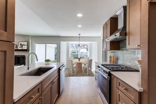 kitchen with wall chimney exhaust hood, appliances with stainless steel finishes, a sink, and light countertops