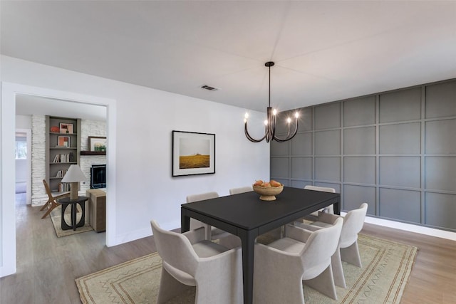 dining room featuring a notable chandelier, visible vents, a large fireplace, wood finished floors, and baseboards