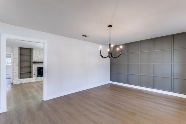 unfurnished room featuring a large fireplace, baseboards, built in features, wood finished floors, and a notable chandelier