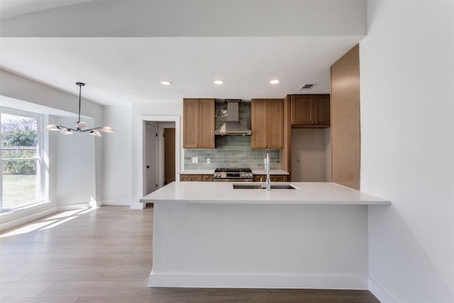 kitchen featuring stainless steel gas range oven, a sink, light countertops, wall chimney exhaust hood, and tasteful backsplash