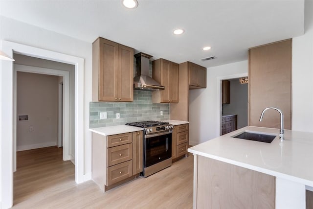 kitchen with visible vents, decorative backsplash, a sink, wall chimney range hood, and stainless steel gas range oven