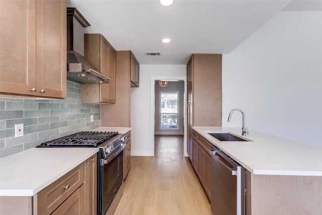 kitchen with stainless steel appliances, a sink, light wood-style floors, wall chimney range hood, and tasteful backsplash