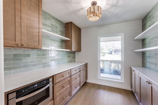 kitchen featuring light wood finished floors, tasteful backsplash, light countertops, stainless steel oven, and open shelves