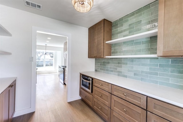 kitchen with open shelves, light countertops, visible vents, backsplash, and light wood-style floors