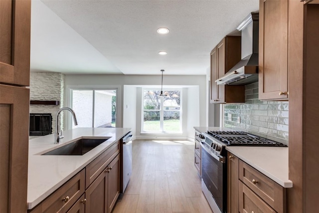 kitchen featuring decorative backsplash, appliances with stainless steel finishes, light wood-style floors, a sink, and wall chimney range hood