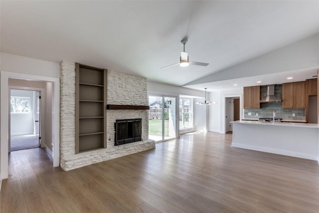 unfurnished living room with wood finished floors, vaulted ceiling, a stone fireplace, a sink, and ceiling fan with notable chandelier