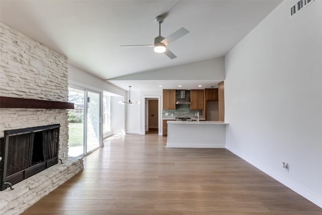 unfurnished living room with lofted ceiling, a stone fireplace, light wood-style flooring, visible vents, and a ceiling fan