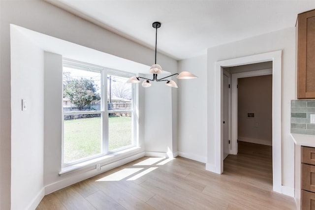 unfurnished dining area with light wood-style floors, baseboards, and a chandelier