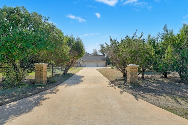 view of property hidden behind natural elements featuring driveway and fence