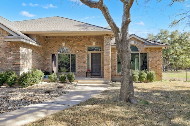 view of front of home with a shingled roof, brick siding, and fence