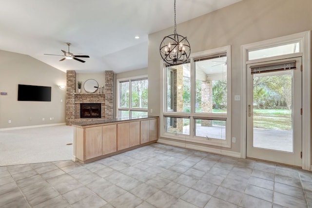 kitchen featuring light brown cabinetry, a large fireplace, open floor plan, vaulted ceiling, and ceiling fan with notable chandelier