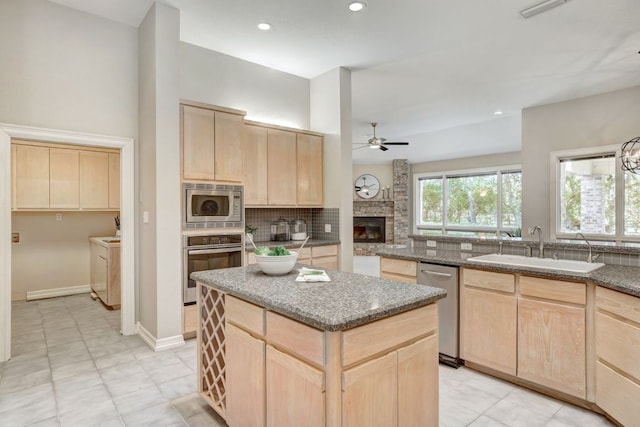 kitchen featuring stone counters, light brown cabinets, stainless steel appliances, a kitchen island, and decorative backsplash