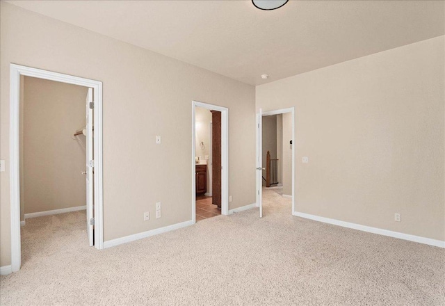 unfurnished bedroom featuring ensuite bathroom, light colored carpet, baseboards, a closet, and a walk in closet