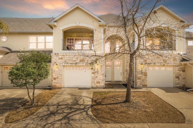 townhome / multi-family property with driveway, a garage, a balcony, stone siding, and stucco siding