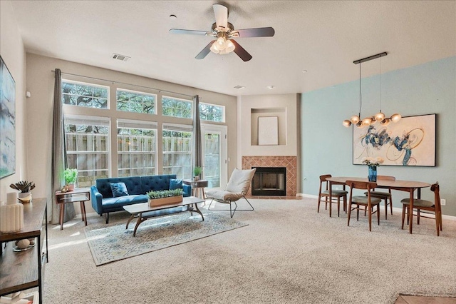 carpeted living area featuring baseboards, visible vents, a tiled fireplace, and ceiling fan with notable chandelier