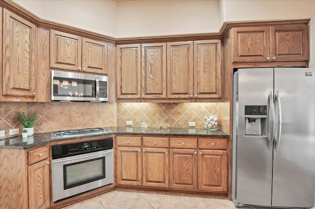 kitchen featuring appliances with stainless steel finishes, dark stone counters, brown cabinets, and backsplash