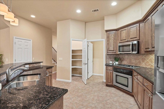 kitchen featuring stainless steel appliances, a sink, visible vents, decorative backsplash, and dark stone counters