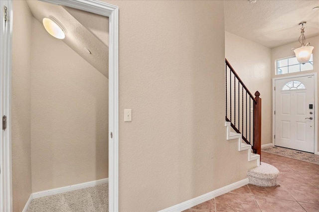 entrance foyer with stairs, a textured ceiling, light tile patterned flooring, and baseboards