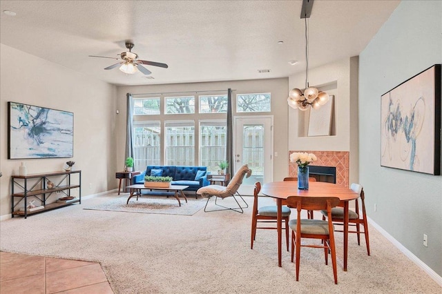 tiled dining space featuring a textured ceiling, ceiling fan with notable chandelier, a fireplace, carpet flooring, and baseboards