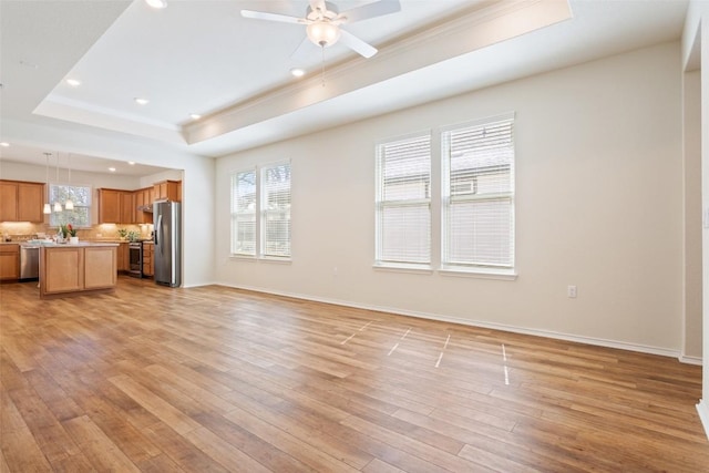 unfurnished living room with light wood finished floors, a tray ceiling, and a healthy amount of sunlight