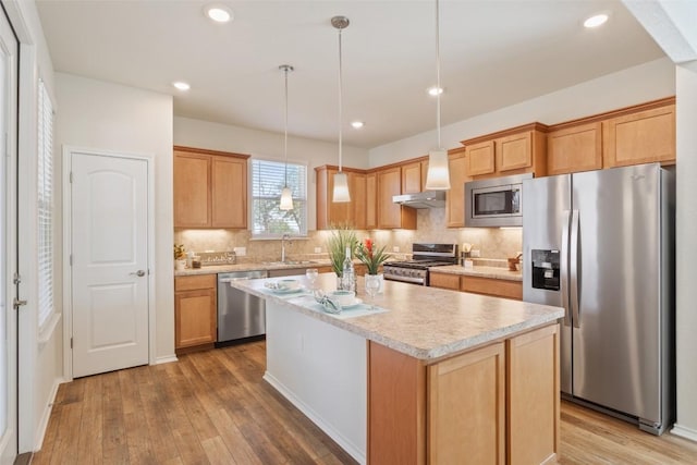 kitchen with stainless steel appliances, tasteful backsplash, light countertops, a sink, and wood finished floors