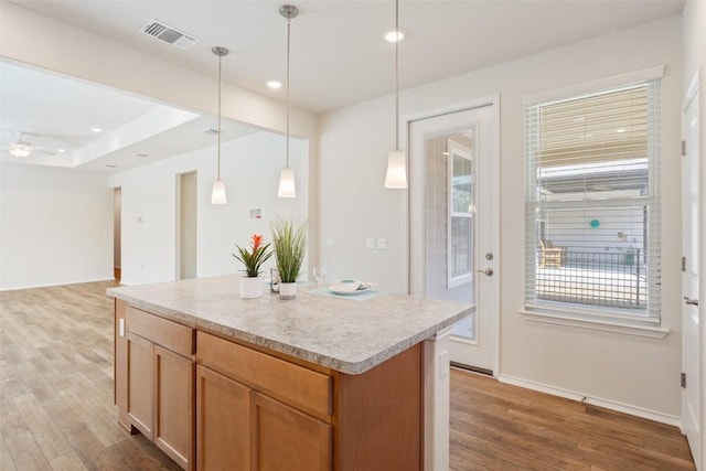 kitchen featuring visible vents, a kitchen island, wood finished floors, hanging light fixtures, and light countertops