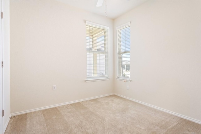 spare room featuring light carpet, a ceiling fan, and baseboards