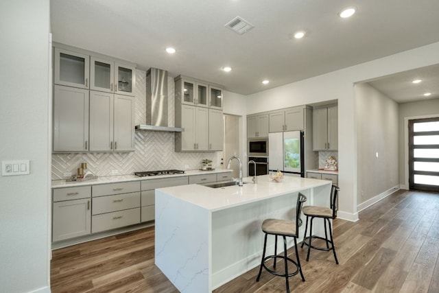 kitchen featuring a sink, stainless steel oven, gray cabinets, wall chimney exhaust hood, and refrigerator