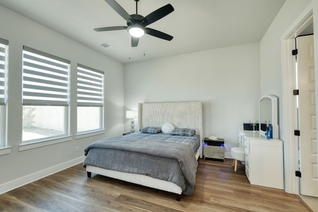 bedroom featuring baseboards, a ceiling fan, wood finished floors, and visible vents