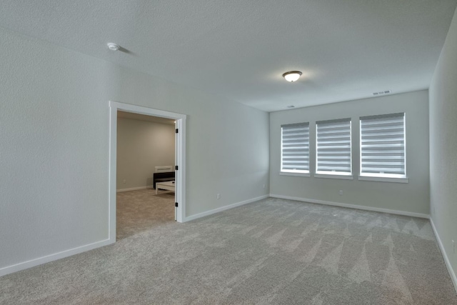 carpeted spare room featuring baseboards, a textured ceiling, and visible vents