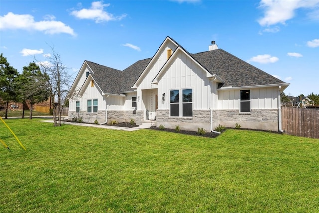 view of front of home with a shingled roof, stone siding, fence, a front lawn, and board and batten siding