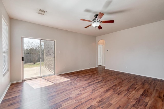 unfurnished room with arched walkways, visible vents, ceiling fan, wood finished floors, and baseboards