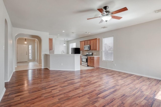 unfurnished living room with arched walkways, visible vents, baseboards, a ceiling fan, and light wood-style floors