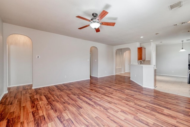 unfurnished living room with arched walkways, ceiling fan, visible vents, baseboards, and light wood-type flooring