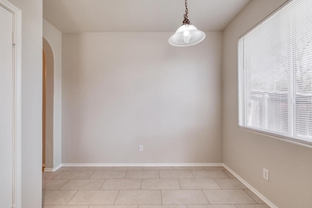 empty room featuring arched walkways, light tile patterned flooring, and baseboards