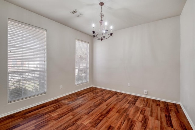 empty room featuring a chandelier, wood finished floors, visible vents, and baseboards