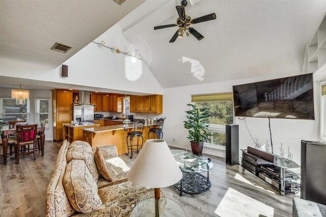 living area with high vaulted ceiling, light wood finished floors, visible vents, and a ceiling fan