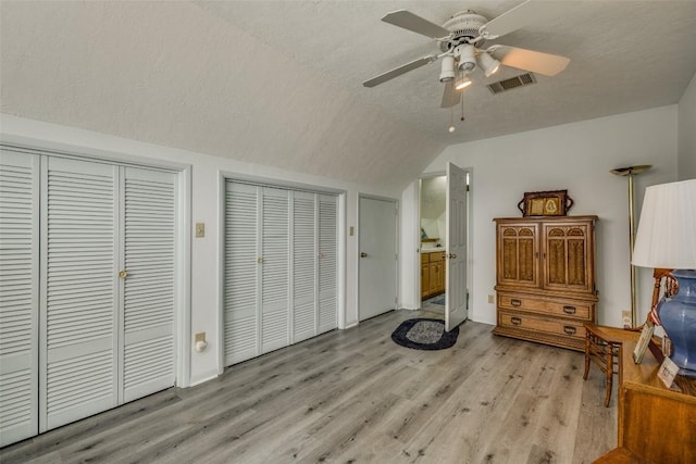 bedroom featuring multiple closets, lofted ceiling, visible vents, light wood-style floors, and a textured ceiling