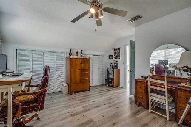 office with a textured ceiling, light wood-style flooring, visible vents, a ceiling fan, and vaulted ceiling