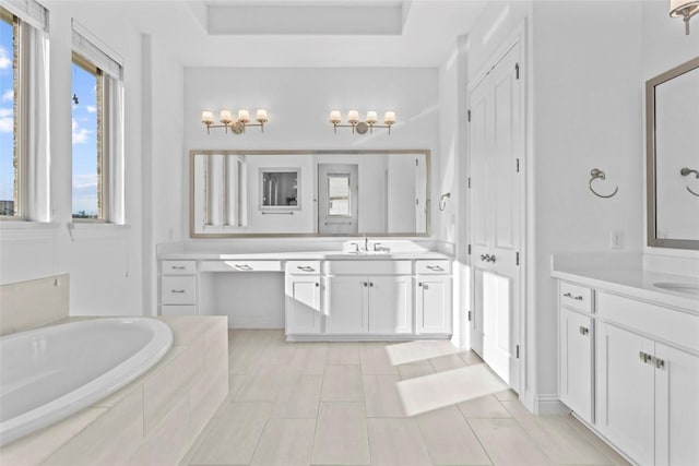 full bathroom featuring a garden tub, a raised ceiling, a sink, and two vanities