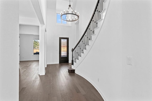 foyer with a towering ceiling, baseboards, stairs, dark wood finished floors, and an inviting chandelier