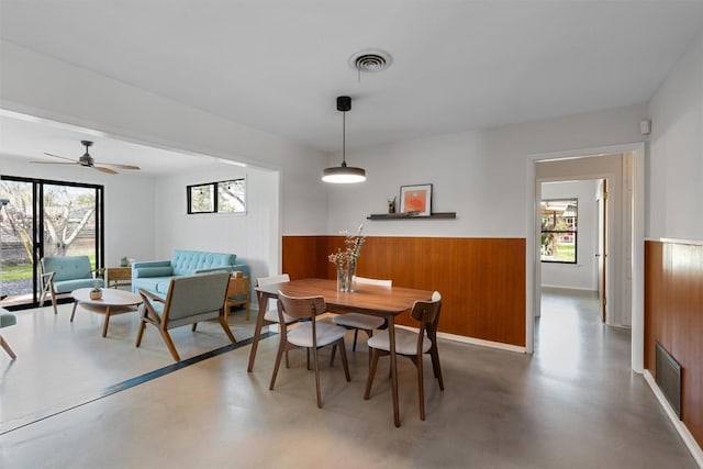 dining space with a healthy amount of sunlight, wood walls, and concrete floors